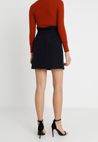 Svart randig kjol med hög midja, tillverkad av texturerad tyg, i kombination med en rostfärgad ribbad tröja och svarta högklackade sandaler.