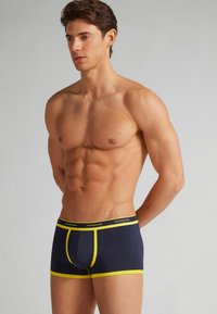 Mörkblå boxerkalsonger med gula detaljer, med resårmidja och en framficka, tillverkade av ett mjukt och stretchigt material.