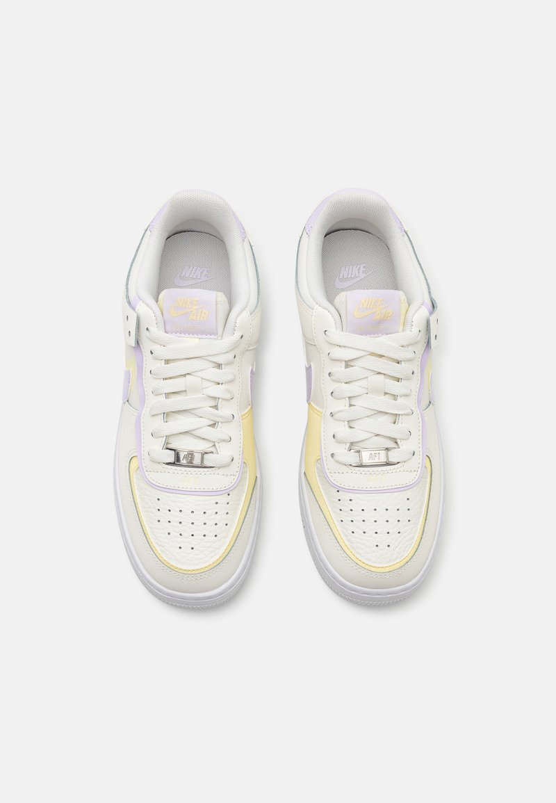 Zapatillas blancas de cuero con acentos en morado claro y amarillo. Cuentan con una puntera perforada, cordones planos y un detalle de logo plateado en la lengüeta.