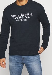 Maglione lavorato a maglia di un blu scuro, con collo a giro e testo bianco "Abercrombie & Fitch New York, N.Y." e polsini e orlo a coste.