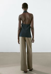 Czarny top na halter z odkrytym plecami w połączeniu z beżowymi spodniami o szerokich nogawkach. Gładka faktura, minimalistyczny design, neutralna paleta kolorów.