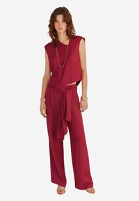 Maroon to-delt outfit med en ærmeløs top og højtaljede, vide bukser med en bundet taljedetalje og blød tekstur.