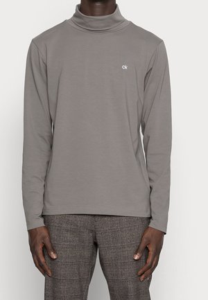 Szary golf z długim rękawem wykonany z gładkiego materiału, z delikatnym logo na lewym piersiu, o luźnym kroju.
