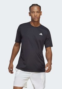 Camiseta atlética negra hecha de tela ligera, con mangas cortas y cuello redondo. Logotipo de la marca en blanco notable en el pecho.