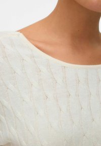 Lekki kremowy sweter dziany z wzorem w warkocz, szerokim dekoltem w kształcie litery U i miękką fakturą. Odpowiedni do noszenia na co dzień.