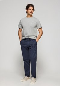 Camiseta de algodón gris de manga corta, chinos azul marino y zapatillas beige claro. Presenta un pequeño logo en la camiseta y detalles en el cinturón.