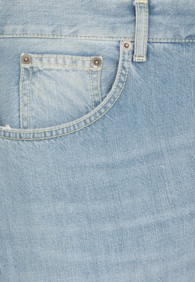 I jeans in denim azzurro chiaro presentano una tasca anteriore curva con hardware argentato e cuciture gialle, evidenziando un tessuto morbido e texturizzato.