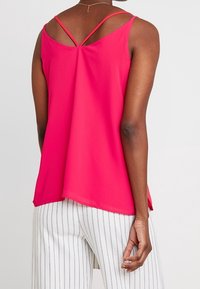 Haut sans manches fuchsia avec des bretelles entrecroisées au dos ; tissu léger qui coule en douceur, complété par une coupe standard.