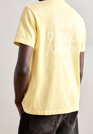 T-shirt en coton jaune à manches courtes, avec un grand texte blanc "MARC O'POLO DENIM" au dos. Coupe régulière et texture lisse.