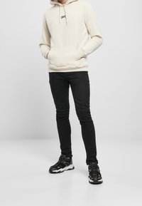 Sweat à capuche crème avec le texte « OFF » en noir, poche avant, associé à un jean noir slim et des baskets noires avec des accents blancs.