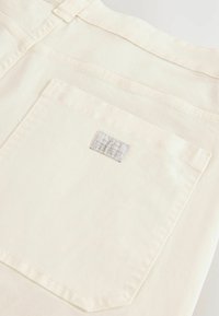 White denim fabric, featuring a single back pocket with a rectangular label. Straight design and subtle stitching details.