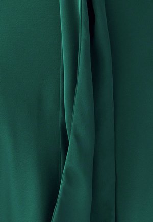 Green fabric with a smooth texture, featuring draped sections and soft folds, highlighting the material's fluidity and sheen.