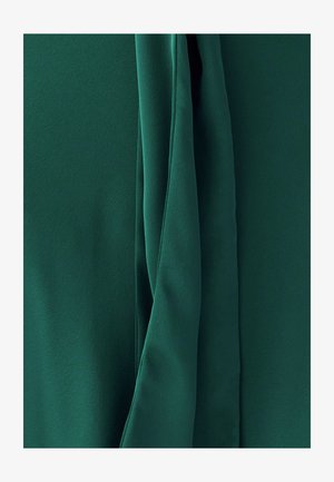 Groen stof met een gladde textuur, voorzien van gedrapeerde delen en zachte plooien, die de vloeibaarheid en glans van het materiaal benadrukken.