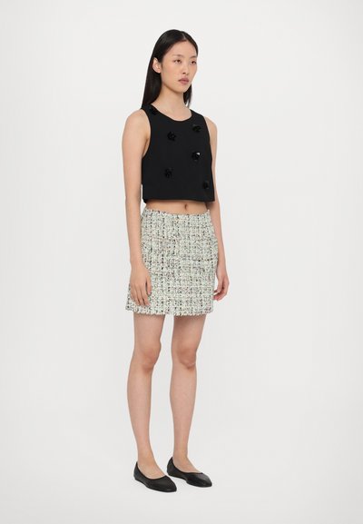 Black crop top with fabric flowers; multi-colored textured mini skirt; flat black shoes; model standing against a plain white background.