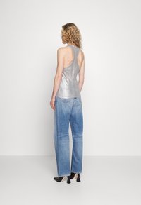 Top sin mangas de color plata con un diseño ajustado. Combinado con unos vaqueros de tiro alto de color azul claro y zapatos negros con detalles de borlas.