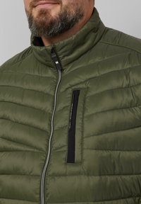 Olivgrüne Daunenjacke mit horizontaler Steppung, hohem Kragen, Reißverschluss und einer schwarzen, rechteckigen Brusttasche. Glatte Textur.