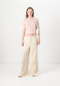 Haut en tricot texturé rose clair à manches courtes associé à un pantalon large crème avec des broderies le long de l'ourlet.