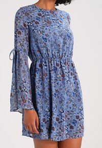 Vestido floral azul con mangas largas acampanadas, cintura fruncida, hecho de una tela ligera que presenta una mezcla de pequeños patrones de flores de colores.