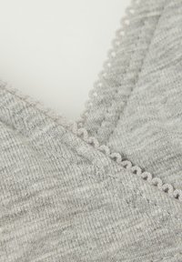 Světle šedá tkanina s měkkou strukturou, se zvlněnými okraji a detailním prošíváním. Design obsahuje jemné variace v odstínu.