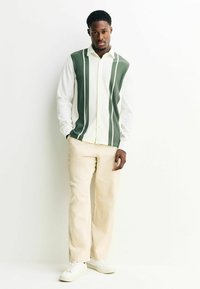 Grün-weiß gestreiftes Hemd mit strukturiertem Design, kombiniert mit beigen Hosen und weißen Sneakers. Einfacher, taillierter Schnitt.