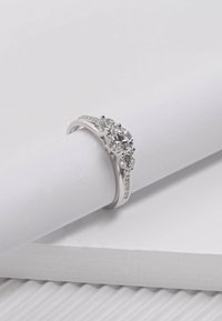 Bague en argent ornée de trois pierres précieuses rondes et transparentes, avec des pierres plus petites le long de l'anneau. Surface lisse et polie avec un design épuré.
