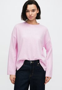 Ανοιχτό ροζ πουλόβερ με στρογγυλή λαιμόκοψη και μακριά μανίκια, με άνετη γραμμή. Συνδυάζεται με σκούρα τζιν παντελόνια, με κλασικό σχέδιο.