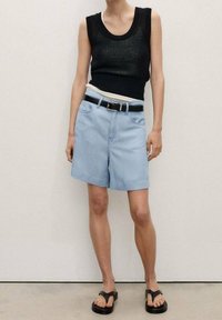 Musta neulottu hihaton toppi, vaaleansiniset denimhousut suoralla leikkauksella ja musta vyö. Mukana myös mustat remmillä varustetut sandaalit.