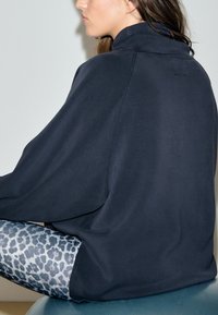 Mørk navyblå oversized sweatshirt med høj krave, glat tekstur og sideslids. Kombineret med mønstrede blå og grå leggings med leopardprint.