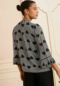 Top bianco e nero con motivo a cuore e chevron, caratterizzato da maniche a tre quarti con dettagli arricciati e una vestibilità comoda.