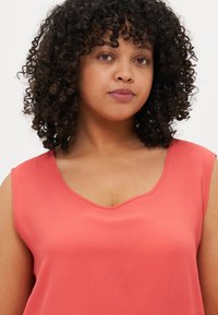 Coral sleeveless top with a V-neckline, made of smooth fabric; features minimal design and a relaxed fit.