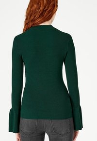 Pull en maille côtelée verte avec manches longues évasées, doté d'un buste ajusté et d'une texture lisse, vu de dos.