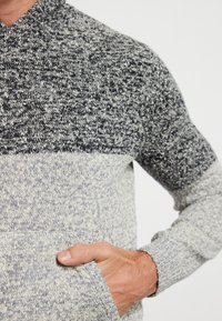 Pullover lavorato a maglia con un design a blocchi di colore grigio e blu navy testurizzato, dotato di un colletto alto e tasche laterali per riporre oggetti.