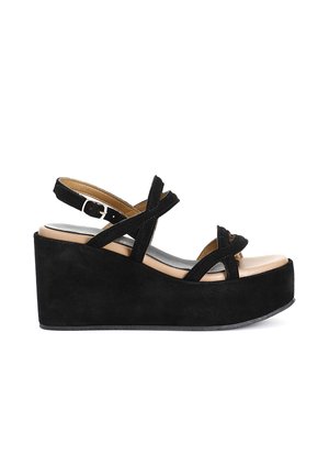 Le sandali con zeppa in suede nero presentano delle cinghie incrociate, una fibbia regolabile alla caviglia e una soletta color nude. La piattaforma testurizzata offre un'altezza aggiuntiva.