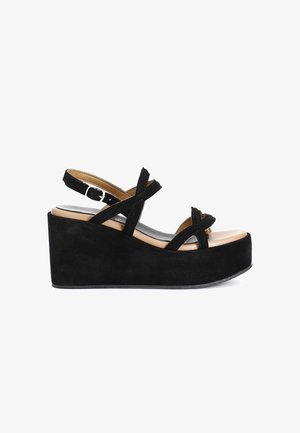 Le sandali con zeppa in suede nero presentano delle cinghie incrociate, una fibbia regolabile alla caviglia e una soletta color nude. La piattaforma testurizzata offre un'altezza aggiuntiva.