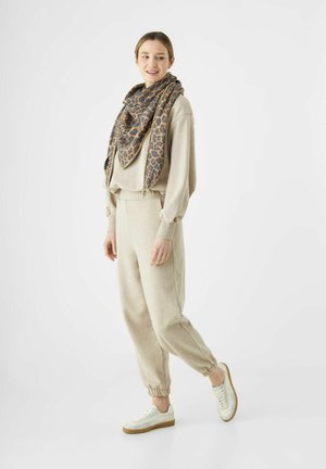 Sweatshirt beige et jogging avec des poignets élastiques, associé à une écharpe à motif léopard. Baskets blanches avec une semelle en gomme.