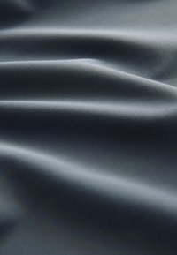 Material textil gri închis cu o textură netedă, prezentând pliuri moi și un luciu subtil, reflectând lumina în diferite zone.