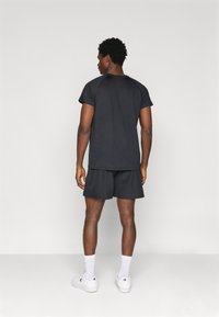 Melns sporta krekls un šorti ar brīvu piegriezumu. Kreklam ir īsas piedurknes, un apģērbs ir kombinēts ar baltām sporta apaviem un zeķēm.