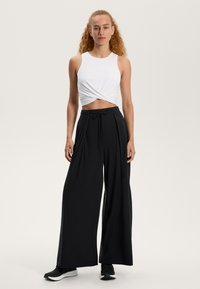 Bela kratka majica s potegom, v kombinaciji z ohlapnimi črnimi širokimi hlačami. Hlače imajo pas z vrvico in gladko teksturo. Črne teniske.