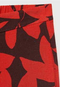 Gros plan sur un tissu rouge avec de grands motifs abstraits de feuilles brun foncé et un détail de couture à la taille élastique.