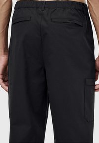 Zwarte cargobroek met een rekbare tailleband, twee achterzakken en een zijzak met een vlak ontwerp. Gladde, lichtgewicht stof.