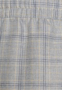 Tejido gris claro con un patrón de cuadros que incluye líneas en azul marino y amarillo. La textura es tejida, con costuras visibles y un ligero brillo.