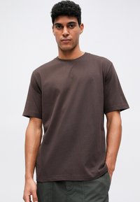 Brun bomull t-shirt med korta ärmar, rundad halsringning och en liten logotypdetalj på bröstet, kombinerad med gröna cargoshorts.