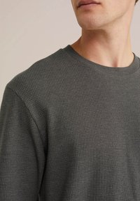 Šedé texturované pletené tričko s dlouhým rukávem a kulatým výstřihem, které má decentní vaflový vzor a žebrované manžety pro dodatečný detail.