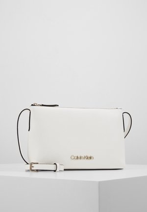 Biała listonoszka Calvin Klein z regulowanym paskiem i złotym logo na gładkiej, fakturowanej powierzchni.