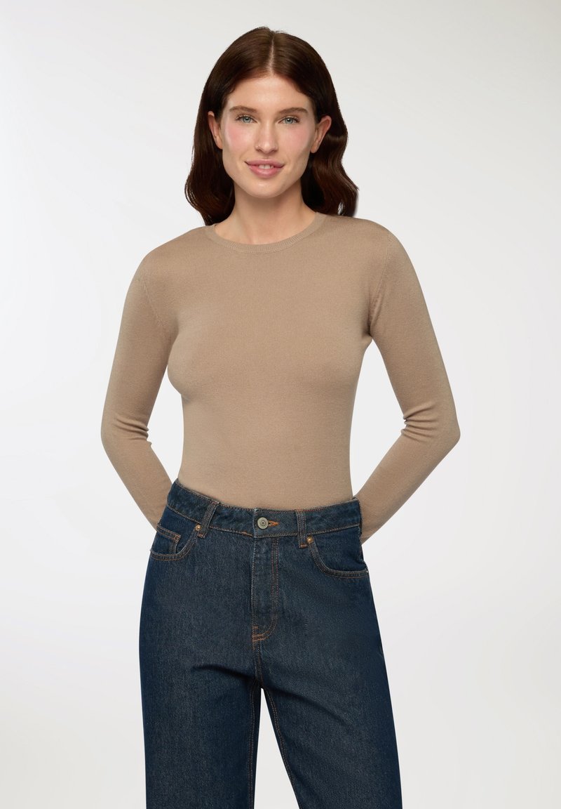 Top beige a maniche lunghe in un design aderente, realizzato in un materiale morbido. Abbinato a jeans a vita alta di colore blu scuro con tasche frontali.