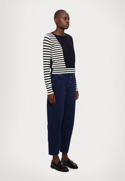 Svart og hvitstripet genser med en solid svart del, kombinert med mørkeblå høytaljede jeans og svarte loafers.
