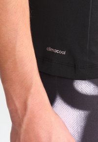Černé sportovní tričko se štítkem "climacool" na spodním lemu. Materiál je hladký a pružný, v kombinaci s vzorovanými legínami.