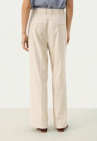 Beige wide-leg trousers with a smooth texture, featuring two back pockets with buttons. Trousers are tailored, with a high waist design.