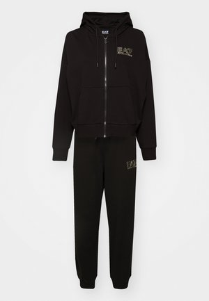 Felpa nera con zip e tasche frontali, dotata di logo; abbinata a pantaloni della tuta neri con logo. Entrambi sono realizzati in tessuto morbido.