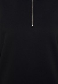 Capo nero con zip, caratterizzato da una texture di tessuto liscia, un colletto alto e una cerniera metallica che accentua l'apertura frontale.